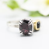 Oval faceted garnet ring in silver bezel and double prongs setting with green tourmaline on the side on sterling silver hammer texture band
