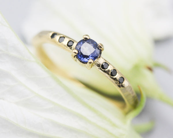 Round faceted blue sapphire ring in prongs setting with tiny black spinel on 14k gold geometric design band