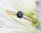 Round faceted blue sapphire ring in prongs setting with tiny diamonds on 14k gold wood texture design band