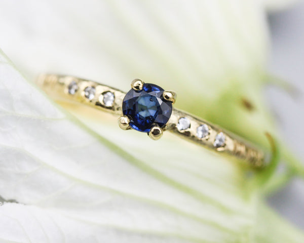 Round faceted blue sapphire ring in prongs setting with tiny diamonds on 14k gold wood texture design band