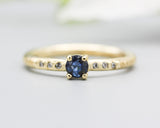 Round faceted blue sapphire ring in prongs setting with tiny diamonds on 14k gold wood texture design band
