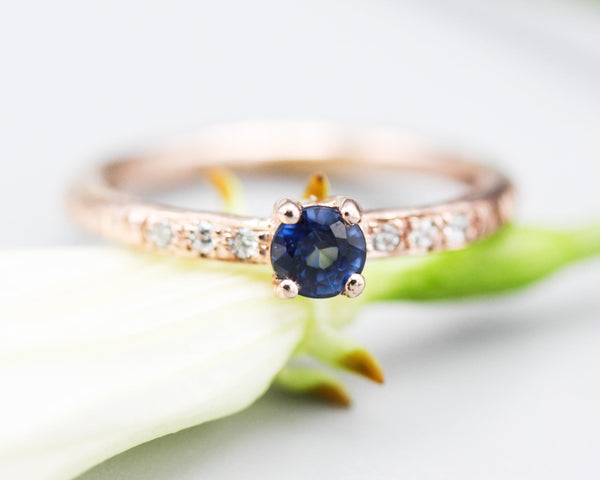 Round faceted blue sapphire ring in prongs setting with tiny diamonds on 14k Rose gold texture design band