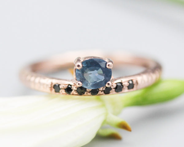 Oval faceted blue sapphire ring in prongs setting with tiny black spinel on 14k Rose gold texture design band