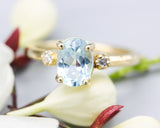 Oval faceted blue topaz ring with tiny round diamonds side set gems in prongs setting with 14k gold half round band