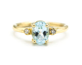 Oval faceted blue topaz ring with tiny round diamonds side set gems in prongs setting with 14k gold half round band