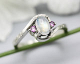Oval cabochon moonstone ring with pink sapphire side set gems in prongs setting with sterling silver oxidized texture band