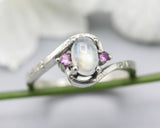 Oval cabochon moonstone ring with pink sapphire side set gems in prongs setting with sterling silver oxidized texture band