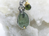 Green kyanite pendant resting on white quartz