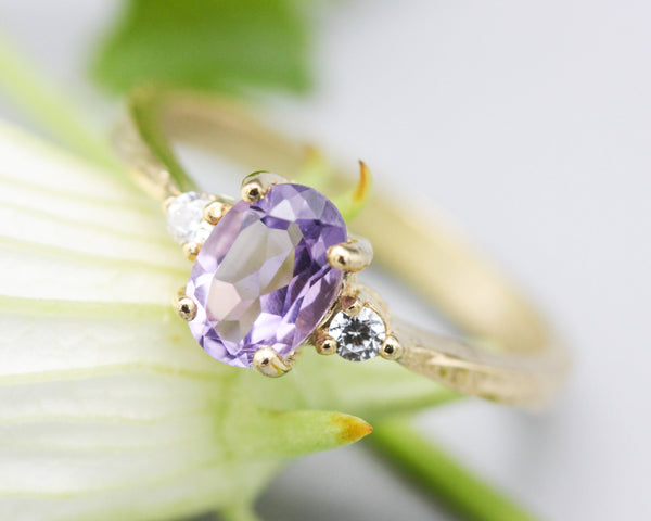 Oval faceted amethyst ring with tiny round diamonds side set gems in prongs setting with 14k gold texture band