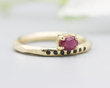 Oval faceted ruby ring in prongs setting with tiny black spinel on 14k gold geometric design band