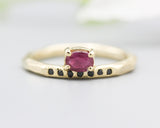 Oval faceted ruby ring in prongs setting with tiny black spinel on 14k gold geometric design band