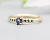 Round faceted blue sapphire ring in prongs setting with tiny black spinel on 14k gold geometric design band