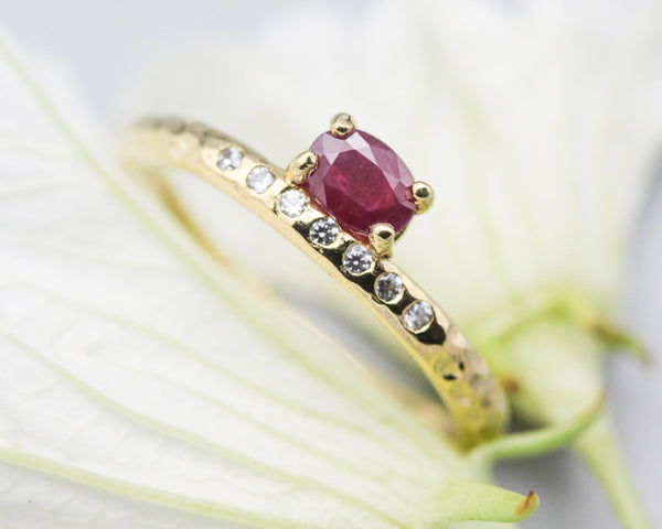 Oval faceted ruby ring in prongs setting with tiny diamonds on 14k gold hammer texture design band
