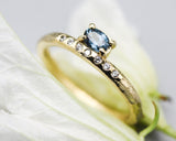 Oval faceted blue sapphire ring in prongs setting with tiny diamonds on 14k gold wood texture design band