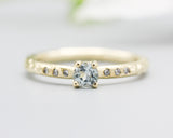 Round faceted blue topaz ring in prongs setting with tiny diamonds on 14k gold hammer texture design band