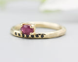 Oval faceted ruby ring in prongs setting with tiny black spinel on 14k gold geometric design band