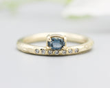 Oval faceted blue sapphire ring in prongs setting with tiny diamonds on 14k gold wood texture design band