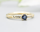 Round faceted blue sapphire ring in prongs setting with tiny diamonds on 14k gold wood texture design band