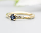 Round faceted blue sapphire ring in prongs setting with tiny diamonds on 14k gold wood texture design band