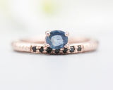 Oval faceted blue sapphire ring in prongs setting with tiny black spinel on 14k Rose gold texture design band