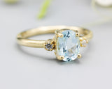 Oval faceted blue topaz ring with tiny round diamonds side set gems in prongs setting with 14k gold half round band