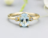 Oval faceted blue topaz ring with tiny round diamonds side set gems in prongs setting with 14k gold half round band