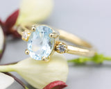 Oval faceted blue topaz ring with tiny round diamonds side set gems in prongs setting with 14k gold half round band