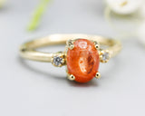 Oval cabochon Sunstone ring with tiny round diamonds side set gems in prongs setting with 14k gold half round band