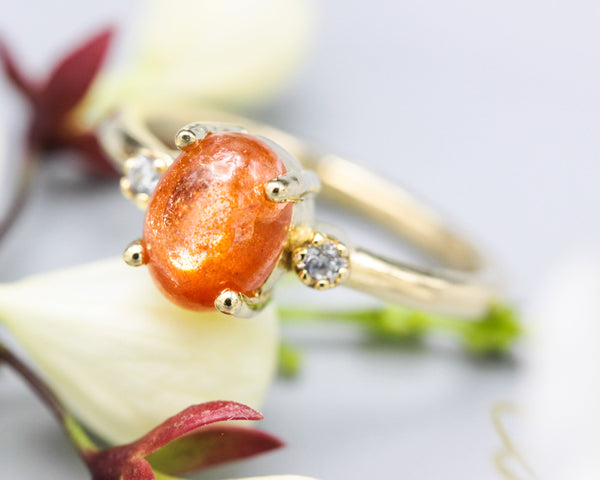 Oval cabochon Sunstone ring with tiny round diamonds side set gems in prongs setting with 14k gold half round band