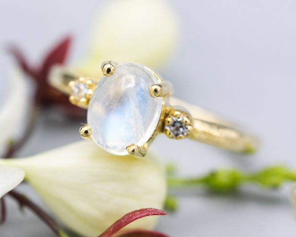 Oval cabochon Moonstone ring with tiny round diamonds side set gems in prongs setting with 14k gold half round band