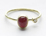 Front view of an oval deep-red stone ring with a small clear accent and textured yellow-tone band