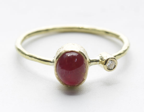 Front view of an oval deep-red stone ring with a small clear accent and textured yellow-tone band
