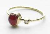 Three-quarter view showing the oval red stone bezel and small round clear accent