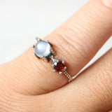Round moonstone ring in silver bezel and prongs setting and tiny garnet on the side with sterling silver twist design band - Metal Studio Jewelry