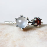 Round moonstone ring in silver bezel and prongs setting and tiny garnet on the side with sterling silver twist design band - Metal Studio Jewelry