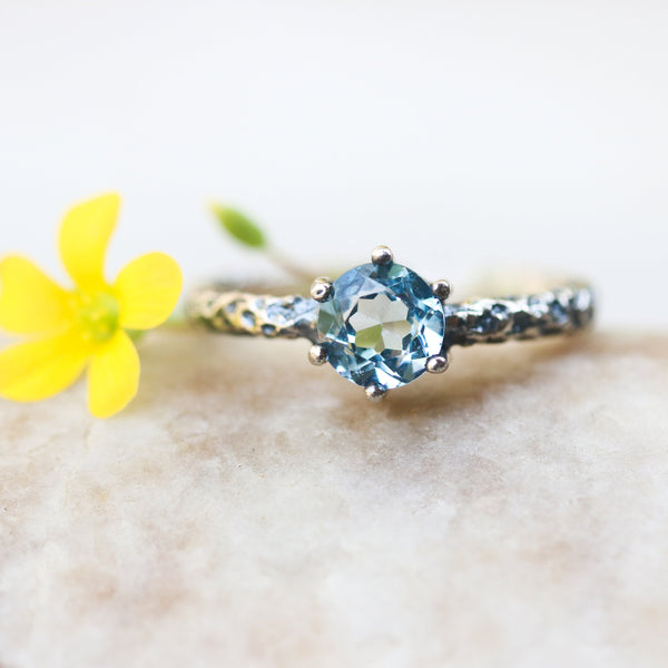 Round faceted Swiss blue topaz ring in silver bezel and prongs setting on sterling silver oxidized hard texture band