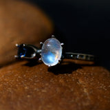 Oval Moonstone ring in silver prongs setting and tiny blue sapphire on the side with sterling silver textured band - Metal Studio Jewelry