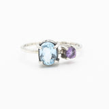 Oval faceted blue topaz ring in silver bezel and prongs setting and tiny amethyst on the side with sterling silver hammer texture band - Metal Studio Jewelry
