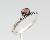Oval faceted garnet ring in prongs setting with tiny black spinel on sterling silver oxidized hammer texture band