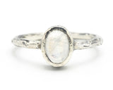 Oval cabochon moonstone ring in sterling silver bezel setting with oxidized textured silver band