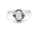 Oval cabochon moonstone ring with pink sapphire side set gems in prongs setting with sterling silver oxidized texture band