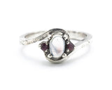 Oval cabochon moonstone ring with tiny ruby side set gems in prongs setting with sterling silver oxidized texture band