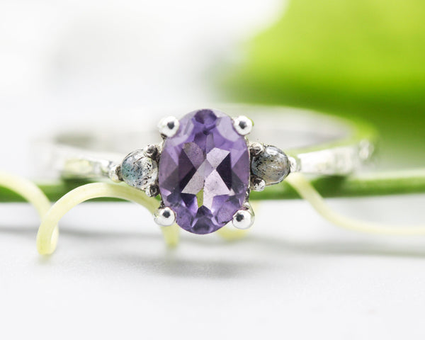 Oval faceted amethyst ring with tiny labradorite side set gems in prongs setting with sterling silver texture oxidized band