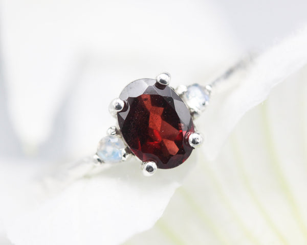 Oval faceted Garnet ring with tiny moonstone side set gems in prongs setting with sterling silver texture oxidized band